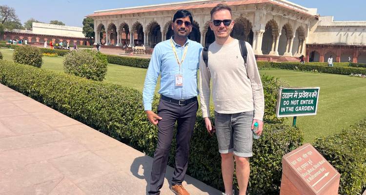 Tour guide and traveller posing in front of an ornate Mughal colonnade surrounded by manicured gardens.