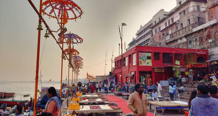Busy ghat scene with decorated umbrellas, devotees and vendors along the riverbank at dusk.