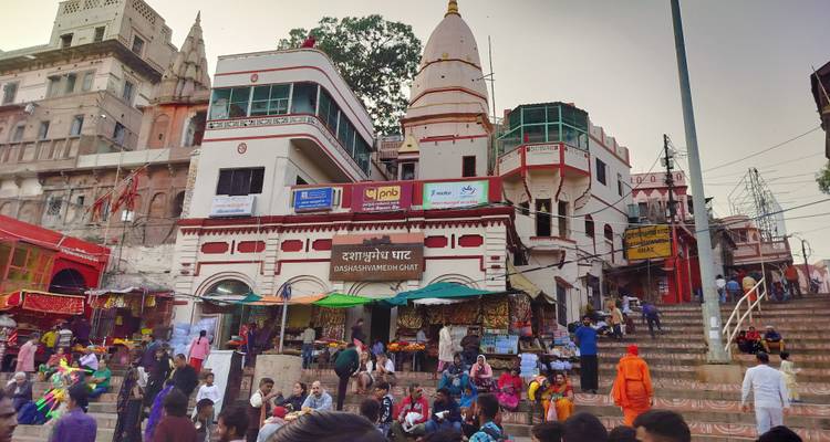 Facade of a temple complex at a ghat crowded with locals, pilgrims and colourful signage.