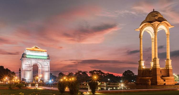 Illuminated war memorial arch and canopy set against a dramatic twilight sky in a landscaped park.