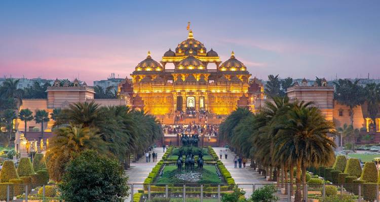 Grand illuminated temple complex with fountains and gardens at dusk.
