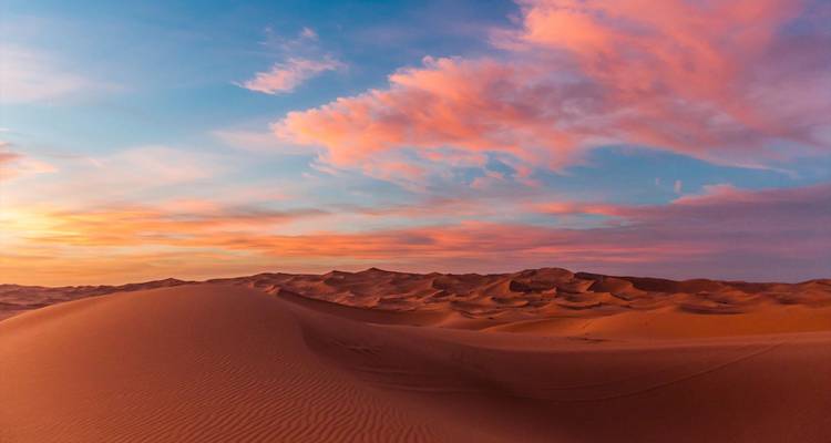 Dunas de arena dorada ondulan bajo un cielo dramático de atardecer rosa y azul en el Sahara