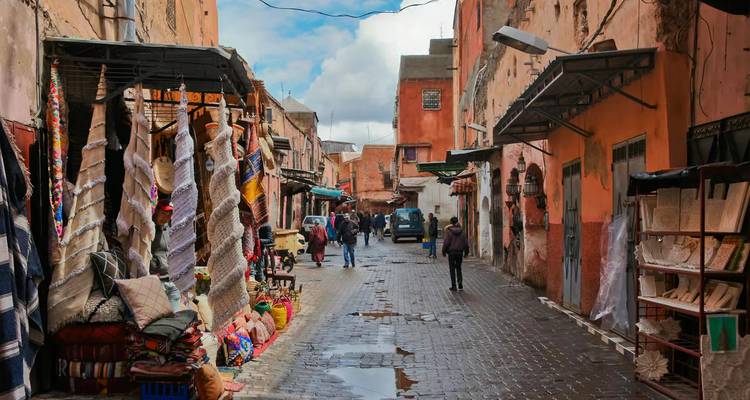Calle estrecha empedrada en Marrakech con puestos de alfombras y textiles después de una lluvia ligera