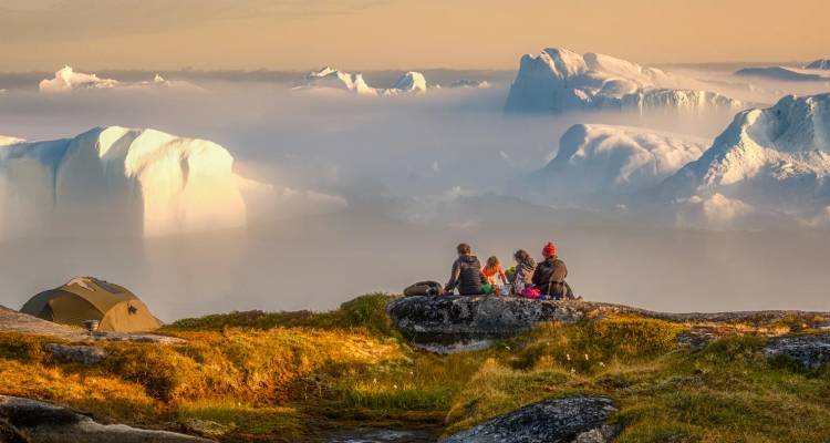 Famille assise sur des rochers couverts de mousse appréciant une vue brumeux de géants icebergs flottant dans le fjord en dessous