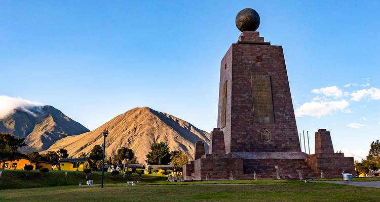 Monument op de evenaar Mitad del Mundo omgeven door groenvoorzieningen en uitlopers van de Andes.