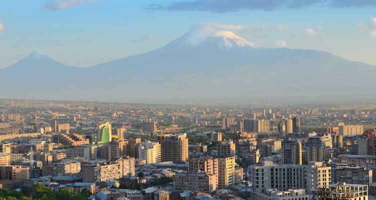 Panoramablick auf den Sonnenuntergang über der Stadt Eriwan mit den Zwillingsgipfeln des Berges Ararat, die in der dunsigen Ferne aufragen.