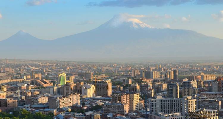 Panoramischer Blick auf die Stadt Jerewan mit dem schneebedeckten Berg Ararat, der sich im Dunst abzeichnet.