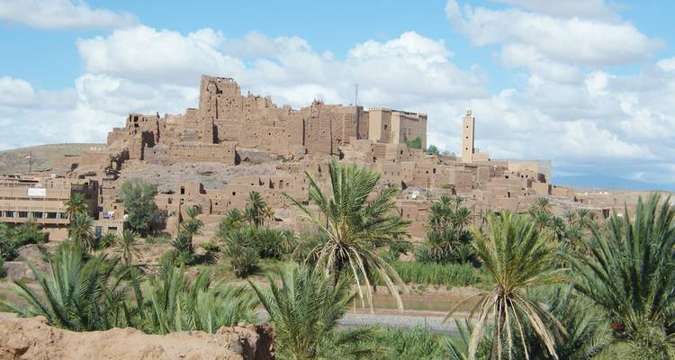 Earthen fortress ruins dominating a palm-dotted valley with river and blue-sky backdrop