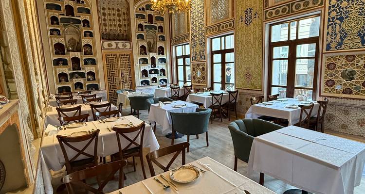 Interior elegante del restaurante decorado con elaborados azulejos uzbekos, lámparas de araña y mesas perfectamente preparadas.