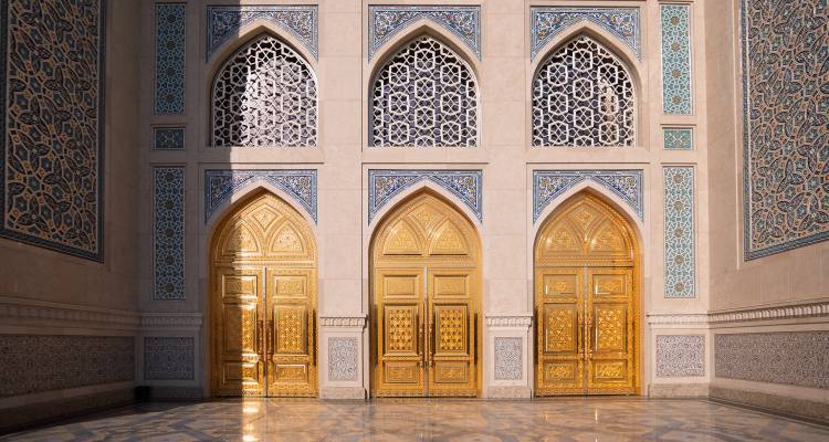 Fachada soleada de una mezquita o madrassa uzbeka ornamentada con puertas doradas y arcos de azulejos azules intrincados