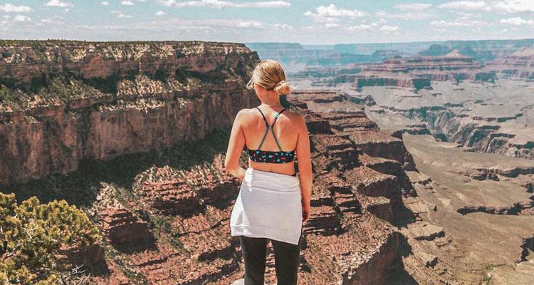 Female hiker stands on cliff edge overlooking the vast layered chasms of the Grand Canyon.