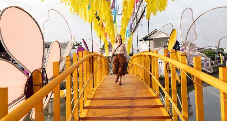 Eine Frau geht über eine lebendige gelbe Fussgängerbrücke, die mit Flaggen und Blumenskulpturen geschmückt ist.