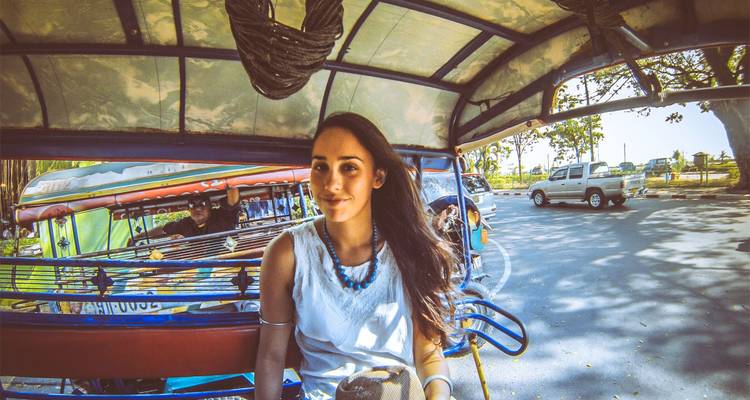 Junger Reisender, der lächelnd in einem farbenfrohen Tuk-Tuk auf einer sonnigen Stadtstraße fährt.