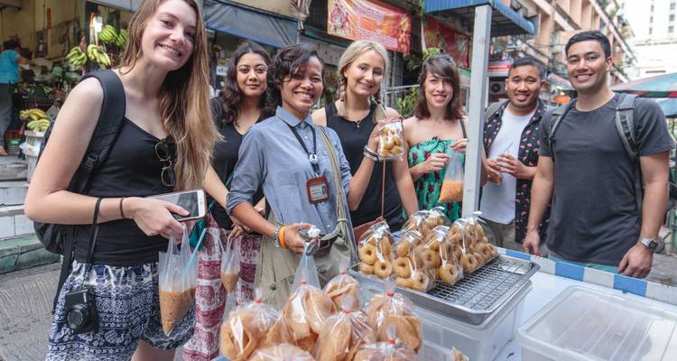 Gruppe von Rucksacktouristen, die frische Straßenmarktsnacks kaufen und neben Tabletts mit frittierten Gebäcken lächeln.