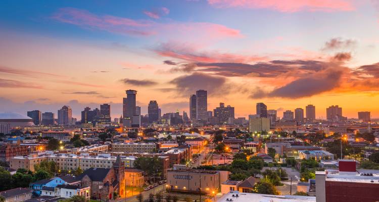 Colorful sunset over the New Orleans skyline with city lights beginning to twinkle.