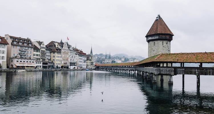 Lucerne’s covered Chapel Bridge stretches across a calm lake toward the stone Water Tower on a gray day.