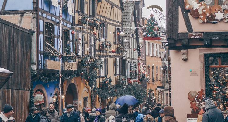 Festive crowds wander a narrow half-timbered street in Colmar decked with Christmas decorations.