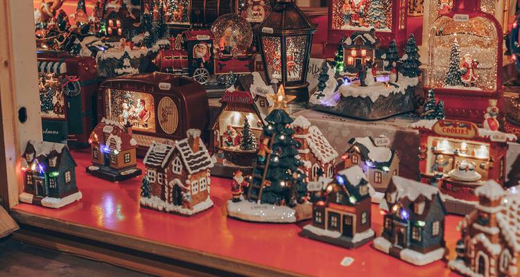 Miniature illuminated Christmas village houses and figurines displayed on a red market stall counter.
