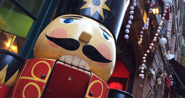 A giant painted nutcracker statue stands by a festive storefront adorned with string lights and ornaments.