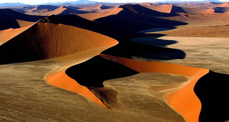 Aerial view of dramatic red sand dunes casting sweeping shadows across a desert valley.