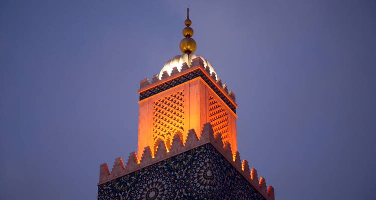 An illuminated mosque minaret with ornate tilework glows against the deepening twilight sky.