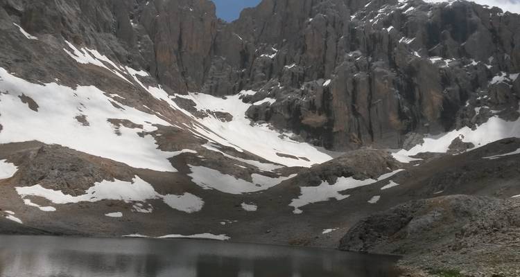 Des plaques de neige s'accrochent aux falaises grises escarpées au-dessus d'un lac alpin immobile haut dans les montagnes du Taurus.