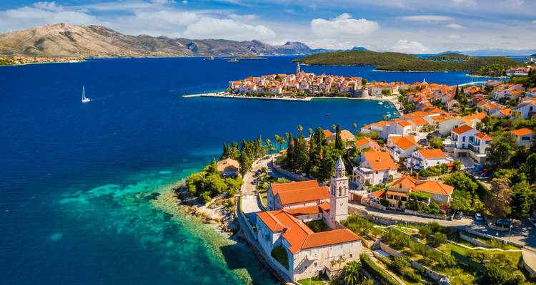 A medieval island town with orange rooftops juts into the sapphire Adriatic Sea surrounded by turquoise coves.