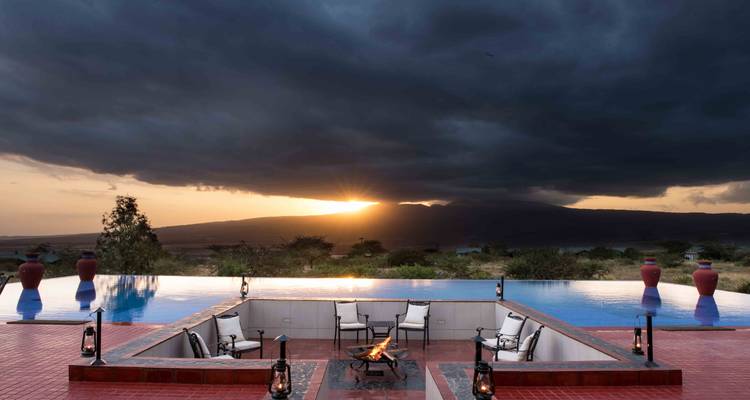 Infinity pool and sunken firepit face a dramatic sunset under stormy skies.