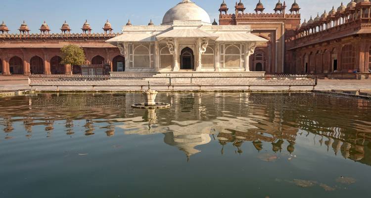 Le tombeau en marbre blanc de Salim Chishti se dresse avec sérénité dans une cour, son reflet scintillant dans le bassin environnant.
