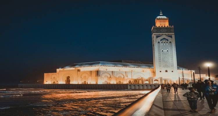 Mosquée Hassan II magnifiquement illuminée la nuit avec des visiteurs se promenant le long de la promenade en bord de mer