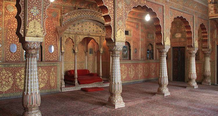 Weelderig versierde binnenhal van Junagarh Fort met rode en gouden patronen en bogen.