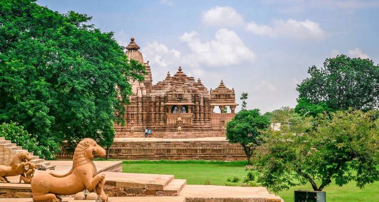 Scenic view of a Khajuraho sandstone temple framed by lush trees and blue sky.