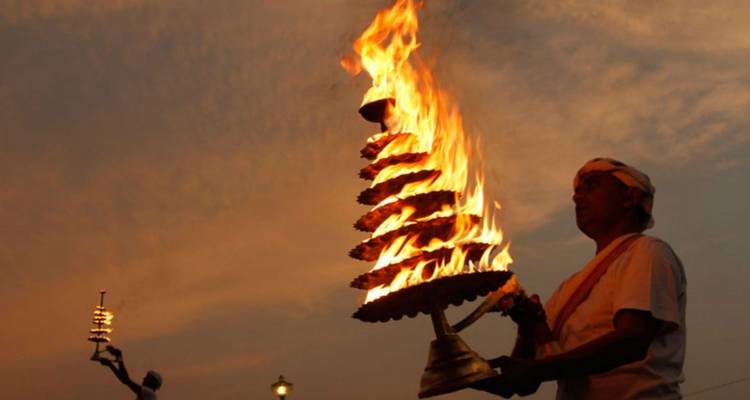 Hindu priest holding a large flaming brass lamp during an evening aarti ceremony.