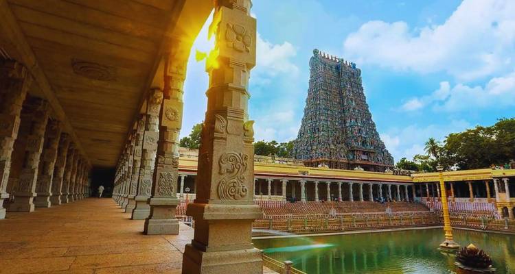 Zonlicht stroomt door een pillarengalerij naar een levendige gopuram naast de tempelvijver in Madurai