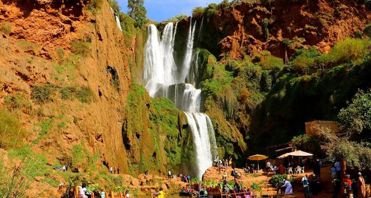 Towering multi-tiered Ouzoud waterfalls cascading into a lush canyon where visitors gather on terraces below