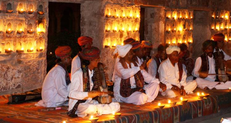 Traditional Rajasthani musicians in colorful turbans perform by candlelight against an ancient stone wall