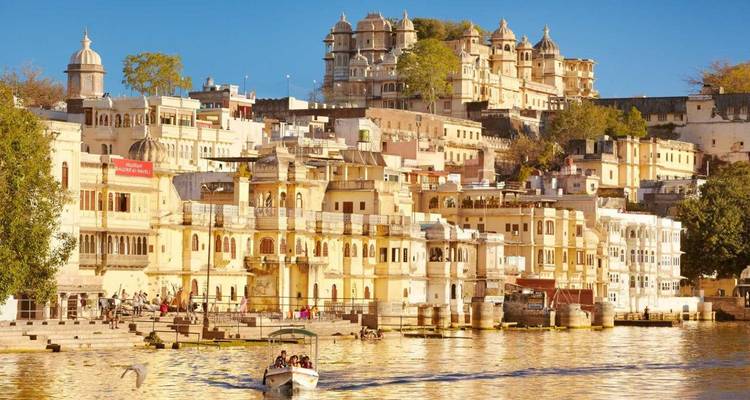 Colorful lakeside facades and palace of Udaipur reflecting in shimmering water with a boat in foreground