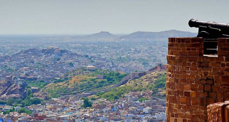 Panoramic cityscape of Jodhpur from fort ramparts with cannon overlooking blue houses and arid hills