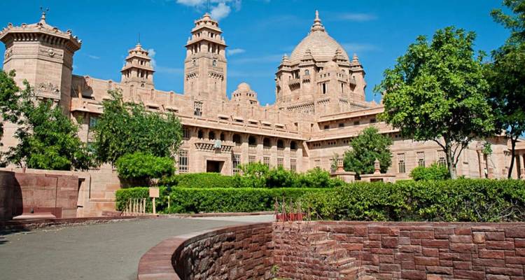 Grand sandstone Umaid Bhawan Palace framed by manicured gardens under a clear blue sky