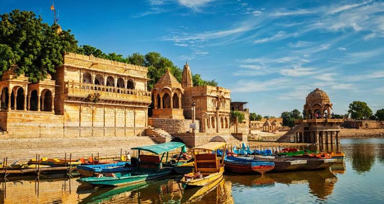 Historic sandstone ghats and temples lining Gadsisar Lake with colorful wooden boats in foreground