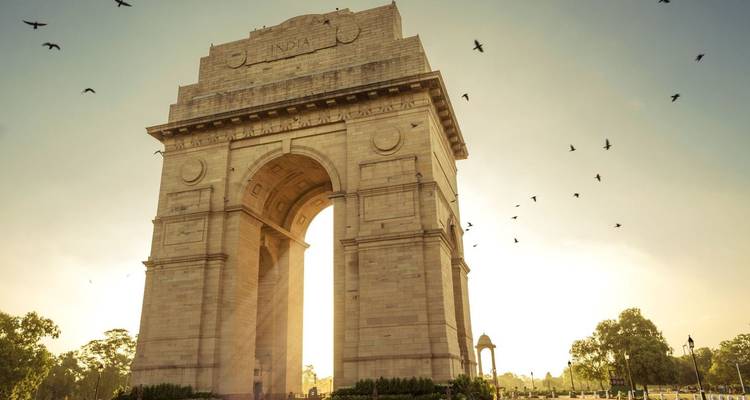 Silhouetted India Gate at golden sunrise with birds flying around the monument