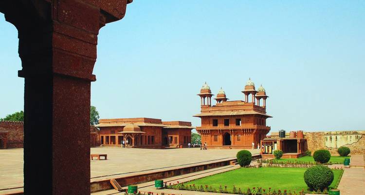 Wide courtyard of red-sandstone palatial buildings with Mughal domes under a clear blue sky