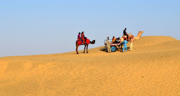 Kameelruiters en kar doorkruisen gouden zandduin onder heldere hemel in Thar-woestijn