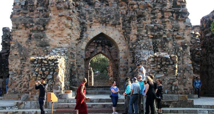 Tourists and a monk explore weathered stone ruins featuring an arched doorway.