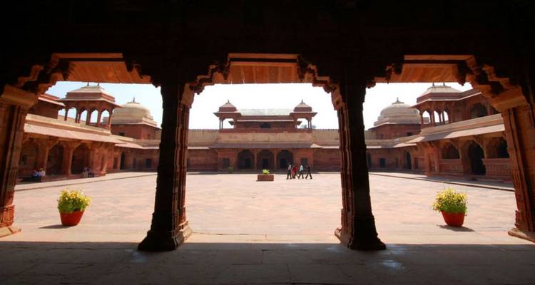 Sun-lit red-sandstone courtyard at Fatehpur Sikri seen through a carved archway.