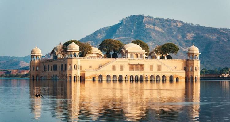 Golden Jal Mahal palace reflected perfectly in calm lake waters with distant hill backdrop.