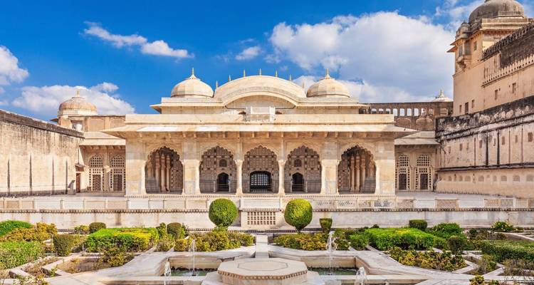 Ornate marble pavilion and lush garden courtyard of Amber Fort under blue sky.