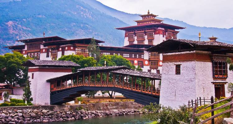 Nahaufnahme der Holzbrücke und gestuften Dächer des Punakha Dzong vor bewaldeten Hügeln