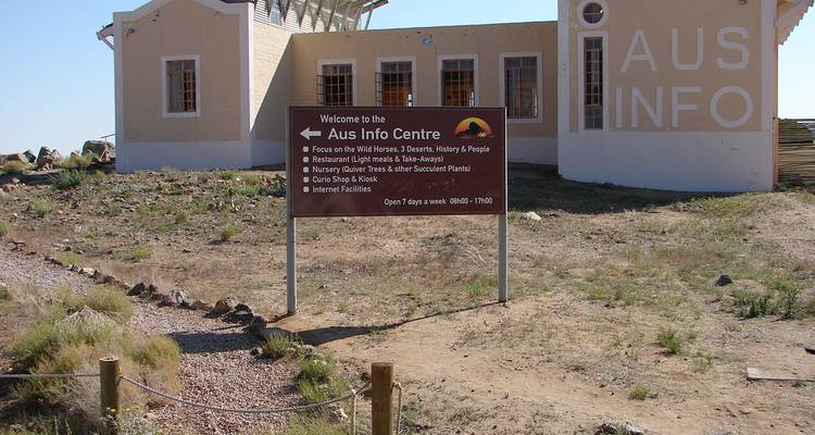 Desert info centre in Aus with a brown welcome sign standing on barren ground beside a small building.