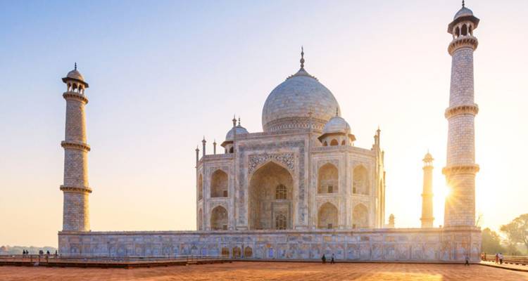 The Taj Mahal bathed in golden sunrise light with long shadows across the red sandstone courtyard.